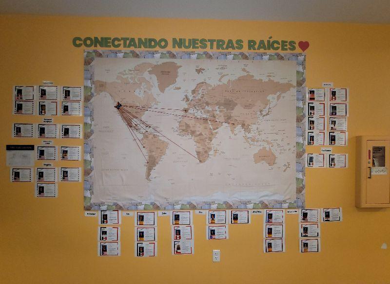 A map of the world on a yellow wall at Arco Iris Spanish Immersion School. The map has strings connecting countries from around the world to Beaverton, Oregon. Above the map a sign reads, “Conectando nuestras raíces.” 